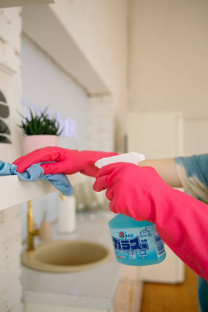 about-04 Person using spray bottle and cloth for cleaning a kitchen shelf, ensuring hygiene and cleanliness.